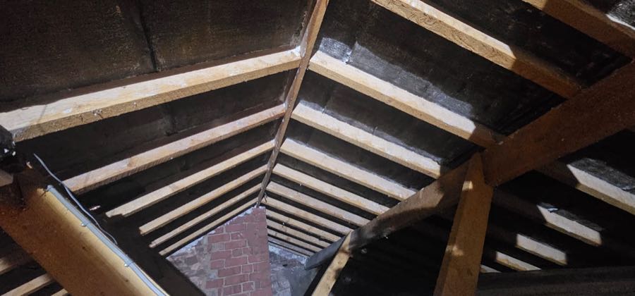 Spray foam insulation removal in progress on a UK roof, rafters exposed